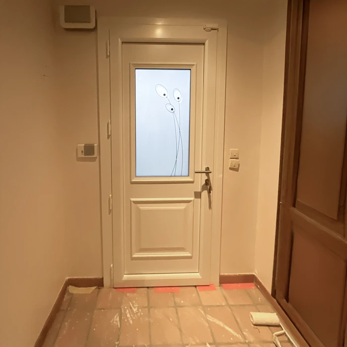 Entrée d'appartement en cours de rénovation avec porte blanche à panneau vitré décoratif et poignée bronze