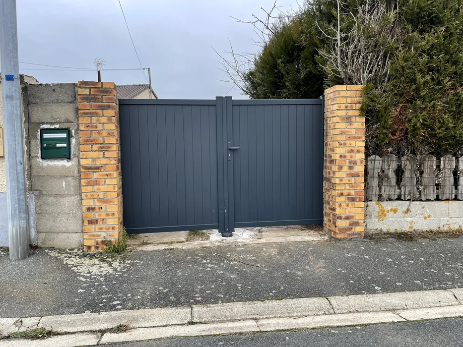 Entrée résidentielle avec portail coulissant gris anthracite à lames verticales, intégré entre piliers en briques oranges