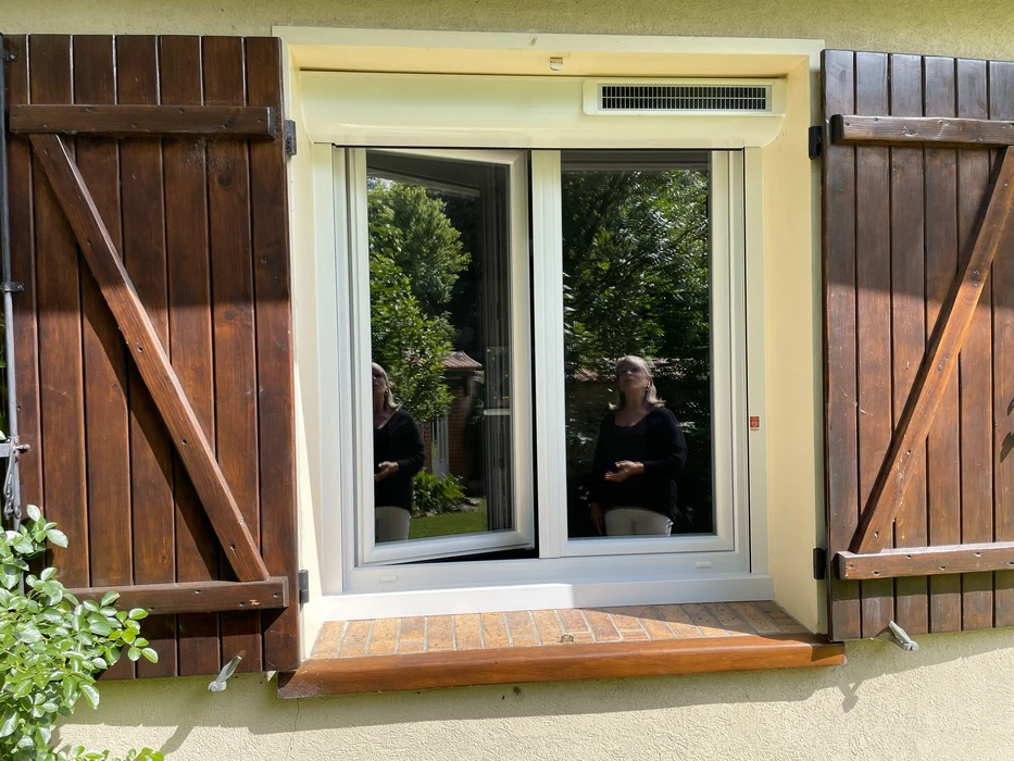 Scène extérieure montrant une femme en vêtement noir assise devant une baie vitrée coulissante moderne
