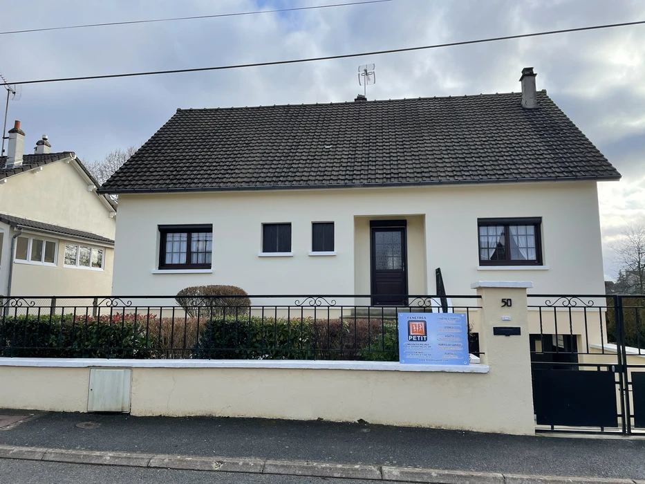 Maison individuelle de plain-pied avec façade blanche, toiture en tuiles grises et menuiseries sombres